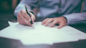 Pessoa assinando um documento sobre a mesa, ilustrando a diferença entre menor assistido e representado