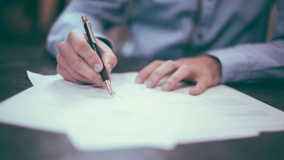 Pessoa assinando um documento sobre a mesa, ilustrando a diferença entre menor assistido e representado