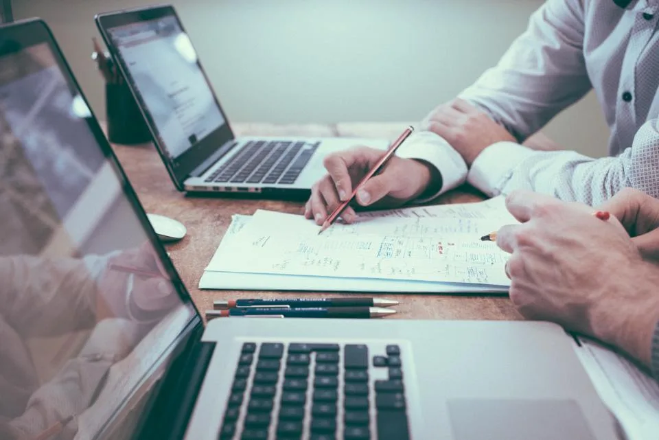 Duas pessoas analisando juntas um documento em papel sobre a mesa de trabalho